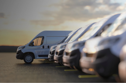 Row of delivery vans parked in a parking lot with a sunset sky.