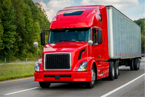 Red truck driving on a road with green trees in the background